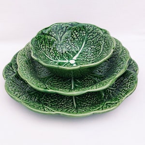 May include: A set of three green ceramic bowls shaped like cabbage leaves. The bowls are nested together, with the smallest bowl on top.