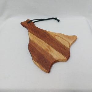 Può includere: Un tagliere in legno con una forma unica e libera e un motivo a venature del legno naturale. Il tagliere ha uno schema di colori marrone scuro e marrone chiaro e un cordino di sospensione verde scuro.