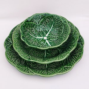 May include: A set of three green ceramic bowls with a cabbage leaf design. The bowls are stacked on top of each other, with the largest bowl on the bottom and the smallest bowl on top.