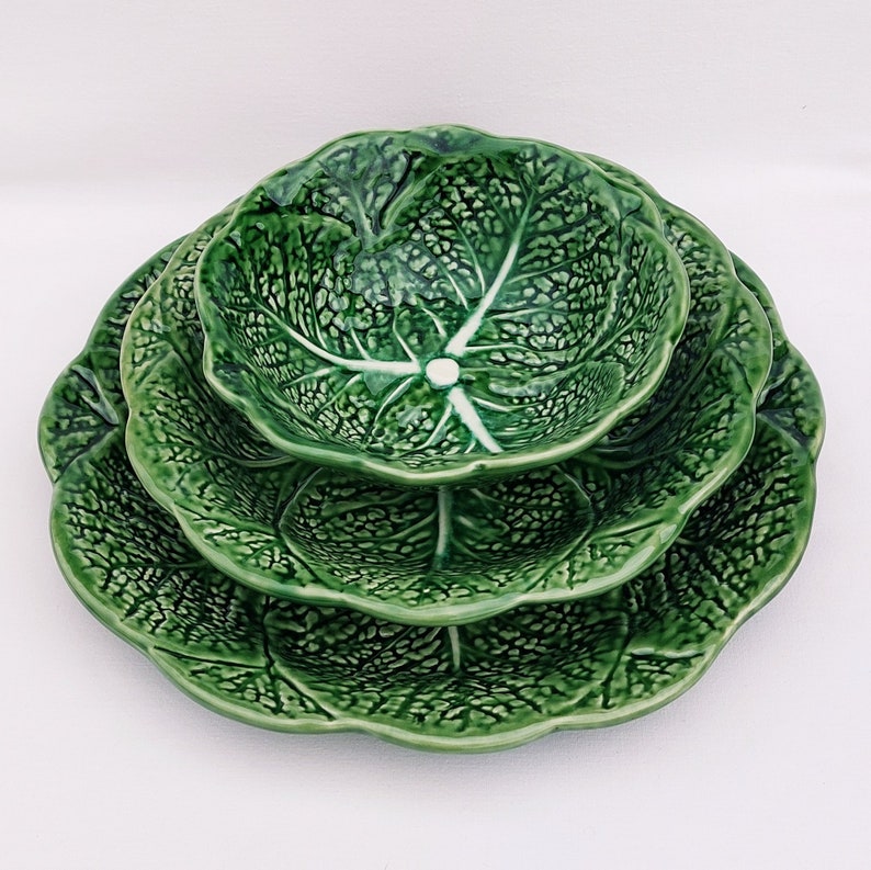 May include: A set of three green ceramic bowls with a cabbage leaf design. The bowls are stacked on top of each other, with the largest bowl on the bottom and the smallest bowl on top.