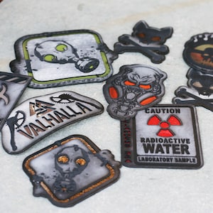 May include: A collection of nine iron-on patches with various designs, including skulls, gas masks, and a warning sign that reads "Caution Radioactive Water Laboratory Sample".