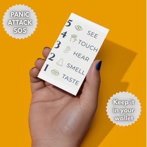 Puede incluir: Una tarjeta blanca con el texto "PANIC ATTACK SOS" y "Keep it in your wallet" sobre un fondo amarillo. La tarjeta enumera los sentidos: Ver, Tocar, O&iacute;r, Oler y Saborear. La tarjeta se sostiene en una mano con esmalte de u&ntilde;as azul.