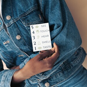 Puede incluir: Una tarjeta rectangular blanca con una lista numerada de los cinco sentidos en tinta verde: 5 SEE, 4 TOUCH, 3 HEAR, 2 SMELL y 1 TASTE, cada uno acompa&ntilde;ado de un icono correspondiente de un ojo, mano, oreja, nariz y boca.