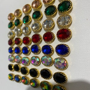 May include: Assortment of oval-shaped rhinestones with gold settings. The rhinestones are arranged in rows by colour, including clear, red, blue, iridescent, black, and green.