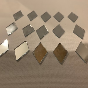 May include: A collection of 14 small diamond-shaped mirror tiles. The tiles are silver and have a reflective surface.