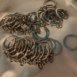 May include: A large pile of silver key rings with a single silver key chain with a silver chain attached.