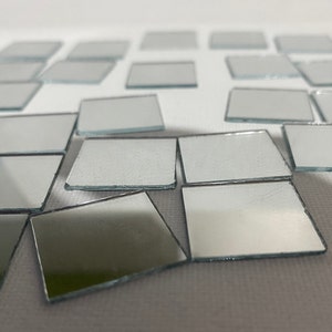 May include: A collection of small, square, silver-framed mirrors scattered on a white surface. The mirrors are arranged in a random pattern, with some overlapping.