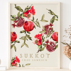 May include: A white framed print with a botanical illustration of pomegranate branches and flowers. The text "Sukkot Chag Sameach" is printed in gold at the bottom of the print.
