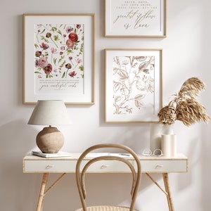 May include: Three framed prints with floral designs and inspirational quotes. The prints are hung on a white wall above a white desk with a wicker chair and a lamp. The quote on the top print reads "So now faith, hope, and love abide these three: but the greatest of these is love."