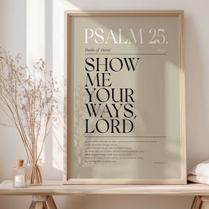 May include: A beige framed print with the text "PSALM 25. Psalm of David. NIV. SHOW ME YOUR WAYS, LORD." The text is in black and the background is a light beige color.