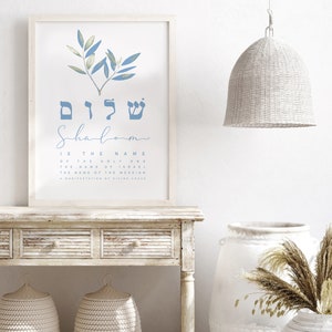 May include: A white framed print with a blue watercolour olive branch design. The Hebrew word "Shalom" is written in blue with the English translation "Shalom is the name of the Holy One, the name of Israel, the name of the Messiah, a manifestation of divine grace."
