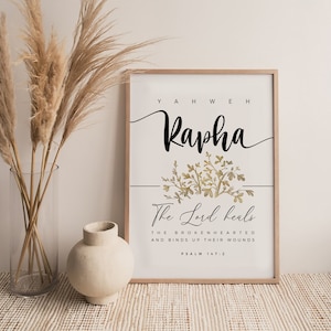 Può includere: Una stampa incorniciata con un motivo floreale dorato e bianco. Il testo recita "YAHWEH Rapha The Lord heals THE BROKENHEARTED AND BINDS UP THEIR WOUNDS PSALM 147:2".