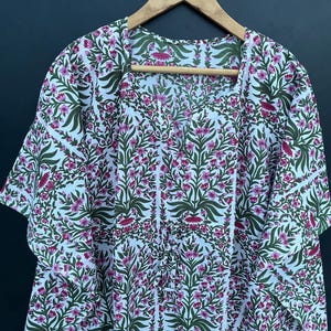 May include: White cotton kimono with a pink and green floral print. The kimono has a V-neck and short sleeves.