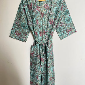 May include: A teal blue robe with a floral print in shades of pink, green, and yellow. The robe has a tie belt and long sleeves.