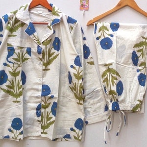 Può includere: Un pigiama bianco con stampa floreale blu. La parte superiore ha una chiusura con bottoni sul davanti e maniche lunghe. I pantaloni hanno una cintura elastica e un cordoncino.