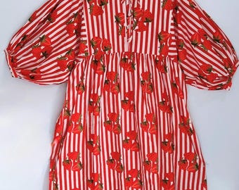 May include: A red and white striped dress with a strawberry pattern. The dress has long, puffy sleeves and a tie at the neckline. The dress is hanging on a wooden hanger.