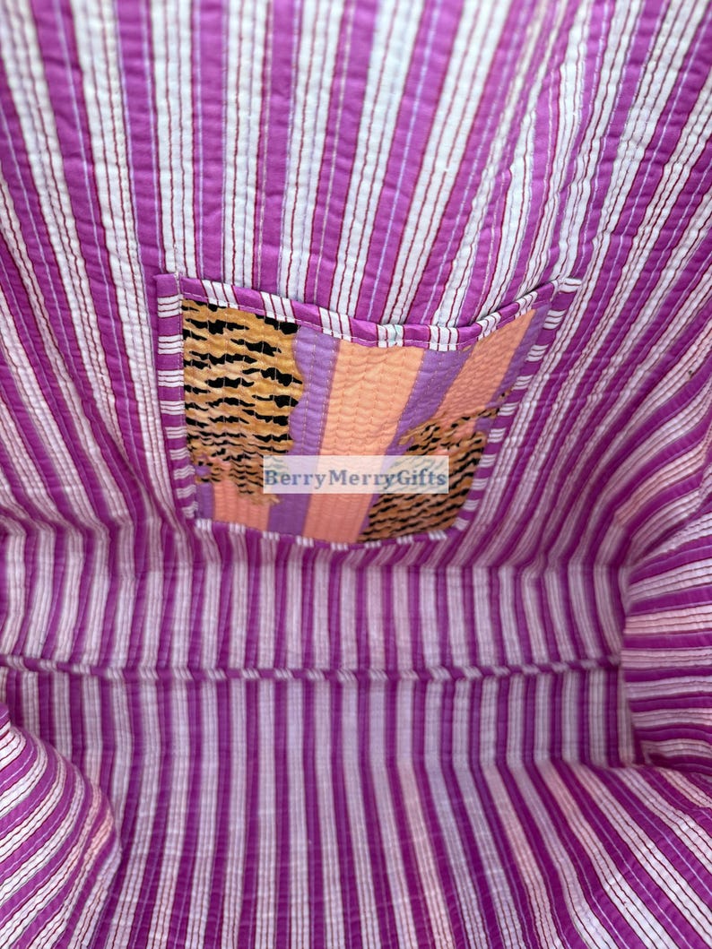 May include: A purple and white striped kantha quilt with a smaller patch of fabric sewn into the center. The patch is made of a variety of fabrics with stripes and patterns in orange, pink, and black. The text "BerryMerryGifts" is visible in the center of the patch.