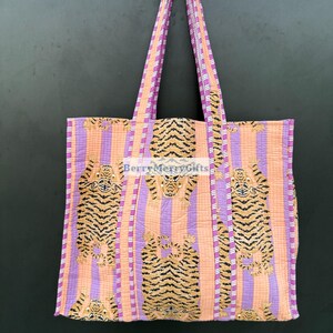 May include: A large tote bag with purple and orange striped fabric. The bag features a repeating pattern of orange tigers on a pink background. The bag has two long straps.