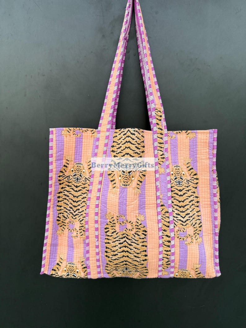 May include: A large tote bag with purple and orange striped fabric. The bag features a repeating pattern of orange tigers on a pink background. The bag has two long straps.