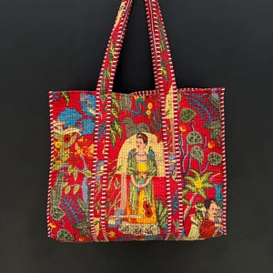 Könnte beinhalten: Rote Tragetasche mit farbenfrohem Blumen- und Figurendesign. Die Tasche zeigt ein zentrales Bild einer Frau in gelbem Kleid und grünem Schal. Die Griffe und Kanten der Tasche sind mit weißen und roten Streifen versehen.