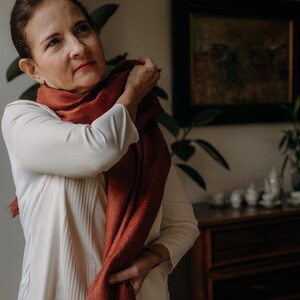 K&ouml;nnte beinhalten: Eine Frau tr&auml;gt eine wei&szlig;e Bluse und einen rostfarbenen Schal. Sie richtet den Schal um ihren Hals.