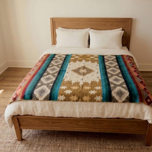K&ouml;nnte beinhalten: Ein Bett mit Holzrahmen und Kopfteil, bedeckt mit einer wei&szlig;en Bettdecke und einer dekorativen Decke. Die Decke zeigt ein geometrisches Muster in Blaugr&uuml;n, Braun, Creme und Orange mit sich wiederholenden Rauten- und Sternmotiven.