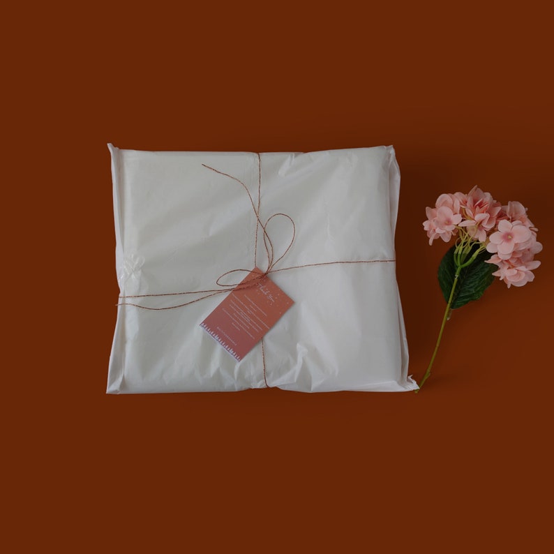 K&ouml;nnte beinhalten: Eine wei&szlig;e Geschenkt&uuml;te, die mit Schnur gebunden ist und einen kleinen Dankesanh&auml;nger hat. Die T&uuml;te liegt auf einem braunen Hintergrund mit einer rosa Blume.