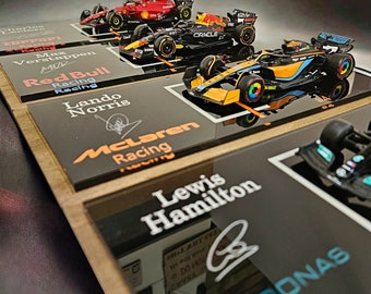 May include: A display case with miniature race cars from Formula 1. The cars are from the teams Red Bull Racing, McLaren Racing, and Petronas. The names of the drivers are listed below each car: Max Verstappen, Lando Norris, and Lewis Hamilton.