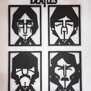 May include: Black wooden wall art featuring stylized portraits of the Beatles band members in individual square frames. The band's name, "The Beatles," is displayed above the portraits in a matching black font. The artwork is mounted on a white wall.
