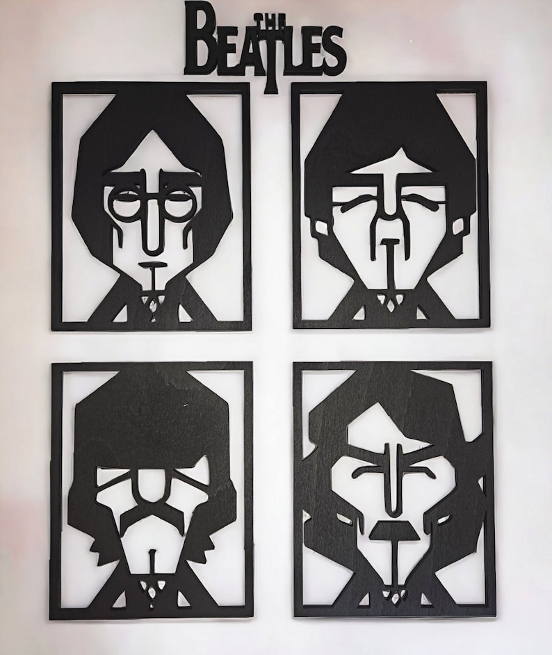 May include: Black wooden wall art featuring stylized portraits of the Beatles band members in individual square frames. The band's name, "The Beatles," is displayed above the portraits in a matching black font. The artwork is mounted on a white wall.
