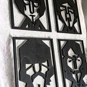 May include: Four black wooden portraits of The Beatles band members in a square frame, with the band's name below. The portraits are cut-out silhouettes with white backgrounds. The Beatles' logo is also black.