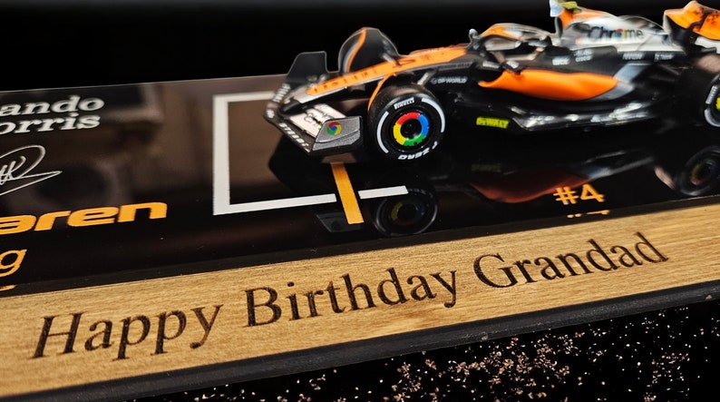 Puede incluir: Un coche de carreras McLaren de F&oacute;rmula 1 a escala en negro y naranja, con el n&uacute;mero 4 y la marca Google Chrome, montado sobre una base negra con el texto Lando Norris, McLaren y el mensaje grabado a l&aacute;ser Happy Birthday Grandad.