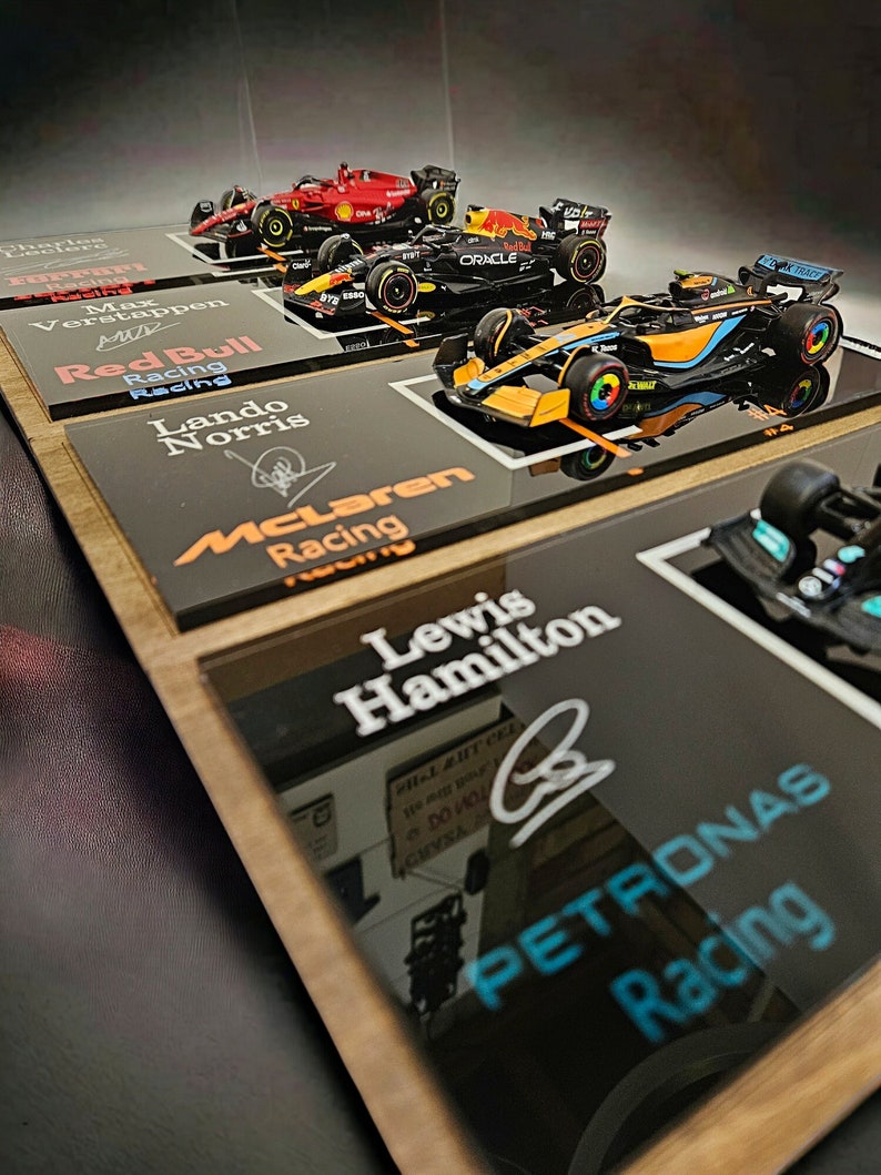 Puede incluir: Una colecci&oacute;n de cuatro modelos de coches de carreras de F&oacute;rmula 1 montados en placas de exhibici&oacute;n individuales. Las placas muestran los nombres Charles Leclerc, Max Verstappen, Lando Norris y Lewis Hamilton, junto con sus logos y firmas.
