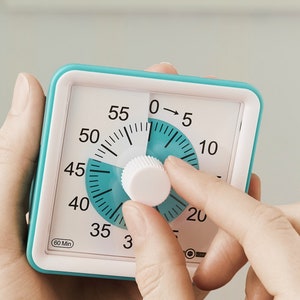 May include: A turquoise and white kitchen timer with a large dial and a knob. The dial has numbers from 0 to 60 and the knob is being turned by a hand. The timer reads "60 Min".