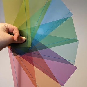 May include: A set of 10 translucent colour filters arranged in a fan shape. The filters are in various shades of green, blue, purple, red, and orange.