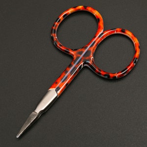 Könnte beinhalten: Kleine Schere mit einer Edelstahlklinge und einem Griff mit Schildpattmuster in Orange, Schwarz und Braun. Diese Schere ist für präzises Schneiden konzipiert und eignet sich für Bastelarbeiten oder Detailarbeiten. Die Gesamtlänge beträgt ca. 10 cm.