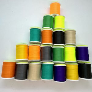 Könnte beinhalten: Eine Sammlung von 18 Garnrollen in verschiedenen Farben, darunter Orange, Grün, Gelb, Schwarz, Lila und Beige. Die Rollen sind in Pyramidenform angeordnet.