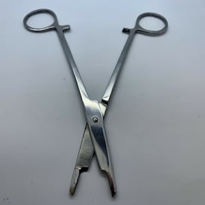 Könnte beinhalten: Eine Zange aus Edelstahl mit gerader Form und einem Verriegelungsmechanismus. Die Zange ist geschlossen und gekreuzt.