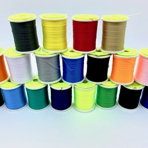 Könnte beinhalten: Eine Sammlung von 18 Garnrollen in verschiedenen Farben, darunter Grün, Blau, Rot, Gelb, Orange, Weiß, Schwarz und Pink. Die Rollen sind in Pyramidenform angeordnet.