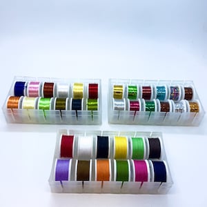 May include: Three clear plastic containers filled with spools of colourful thread. The containers are arranged in a row, with the middle container slightly lower than the others. The spools of thread are arranged in rows and columns, with each spool having a different colour.