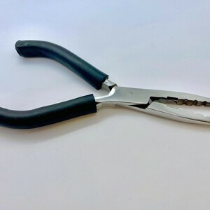 Peut inclure: Pince de pêche en argent avec des poignées en caoutchouc noir. La pince a une mâchoire dentelée et une poignée à ressort.
