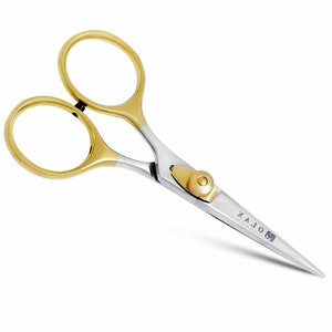 Könnte beinhalten: Kleine, silberne Schere mit goldfarbenen Griffen und Akzenten. Die Schere hat eine spitze Spitze und eine kleine Schraube in der Nähe des Drehpunktes. Der Text "X A J O" ist auf der Klinge aufgedruckt.