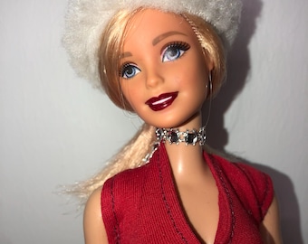 May include: A blonde doll wearing a white beret, a red sleeveless dress, and a silver rhinestone choker. The doll has blue eyes and red lipstick.