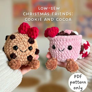 May include: Two crocheted plush toys: a cookie and a cocoa cup. The cookie is tan with brown chocolate chips and a red bow. The cocoa cup is pink with a red and white striped handle and a red bow. The text says "Christmas Friends: Cookie and Cocoa".