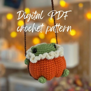 May include: A crocheted pumpkin-shaped plush toy with a green frog face and white crocheted ruffle. The toy is hanging from a string and the text "Digital PDF crochet pattern" is visible above the toy.