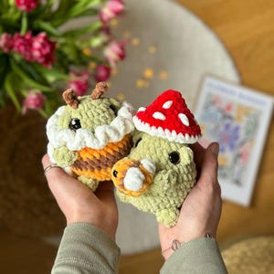 May include: Two crocheted stuffed toys, one resembling a bee with yellow and brown stripes and a white crocheted hat, and the other resembling a mushroom with a red crocheted cap and a green body.