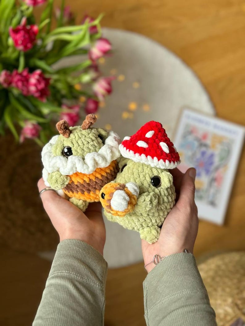 May include: Two crocheted stuffed toys, one resembling a bee with yellow and brown stripes and a white crocheted hat, and the other resembling a mushroom with a red crocheted cap and a green body.