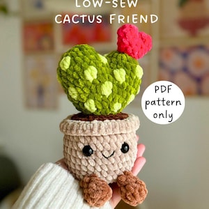May include: A handmade crochet cactus friend in a pot. The cactus is heart-shaped, green with yellow spots, and topped with a red heart. The pot is beige with brown feet and a smiling face. Text on the image says "LOW-SEW CACTUS FRIEND" and "PDF pattern only."