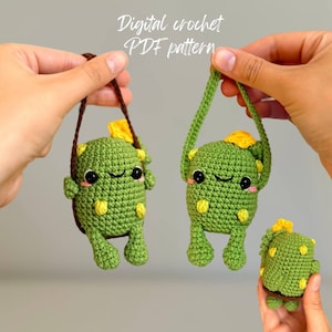 May include: Three crocheted cactus toys with smiling faces. The two larger cacti are hanging from brown and white yarn. The smaller cactus is green with yellow accents. Digital crochet PDF pattern.