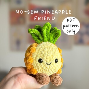 May include: A crochet pineapple plushie with a yellow textured body, green leafy top, and brown feet. The face features black safety eyes and a stitched smile. Text on the image reads: NO-SEW PINEAPPLE FRIEND and PDF pattern only.